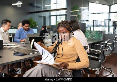 Stressed businesswoman examining documents with colleagues working in background Stock Photo