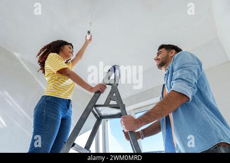 Smiling man helping woman in installing light bulb at home Stock Photo
