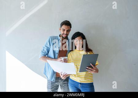 Happy couple using tablet PC and analyzing blueprint in new home Stock Photo
