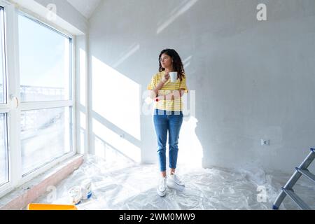 Young woman with coffee cup standing in room under renovation Stock Photo