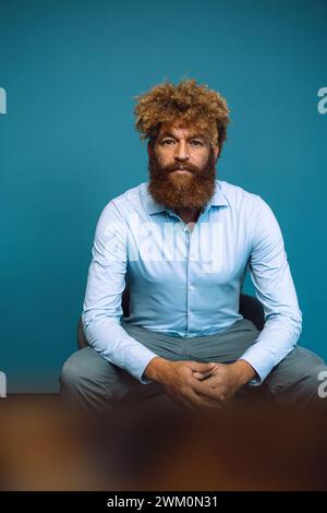 Mature businessman sitting in front of blue wall Stock Photo