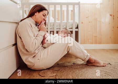 Mother sitting on floor and kissing daughter's feet at home Stock Photo