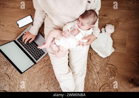Freelancer working on laptop with baby girl sleeping at home Stock Photo