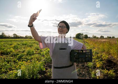 Smiling farmer taking selfie with vegetable crate through smart phone at farm Stock Photo