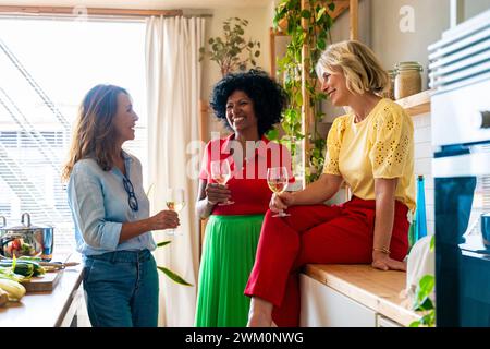 Happy multiracial friends holding wineglasses and talking in kitchen at home Stock Photo