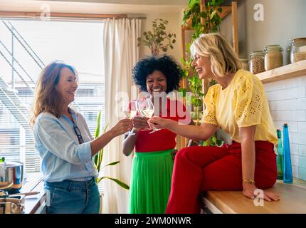 Cheerful multiracial friends toasting drinks in kitchen at home Stock Photo