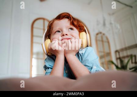 Thoughtful boy listening to music through wireless headphones at home Stock Photo