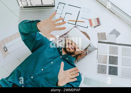 Smiling interior designer wearing VR glasses and lying on floor at office Stock Photo