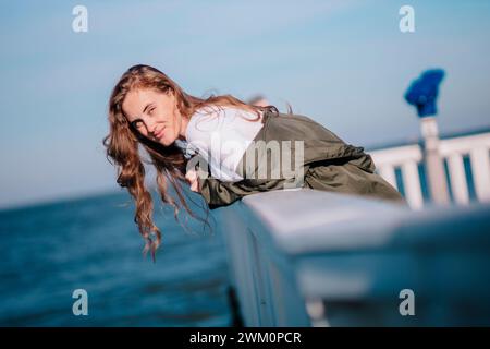 Smiling redhead woman leaning on railing by the sea Stock Photo