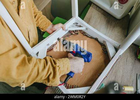 Man using screwdriver drill machine on chair at table Stock Photo