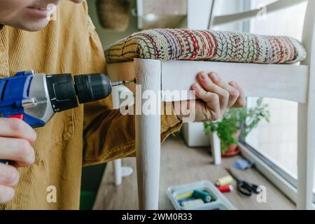 Man using screwdriver drill on chair at home Stock Photo