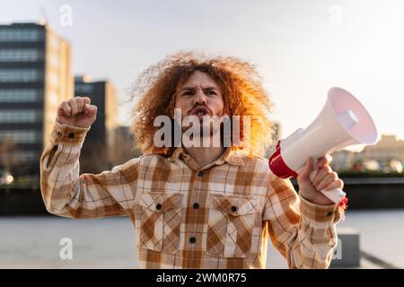 Angry man shouting with megaphone under sky Stock Photo