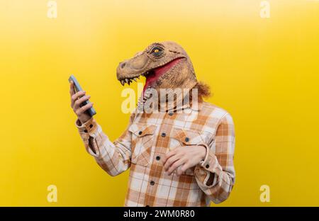 Man wearing dinosaur mask and using smart phone in front of yellow wall Stock Photo