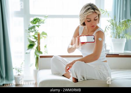 Woman with diabetes measuring blood sugar level through smart phone app at home Stock Photo