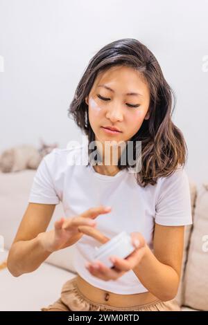 Young woman applying moisturizer on face at home Stock Photo