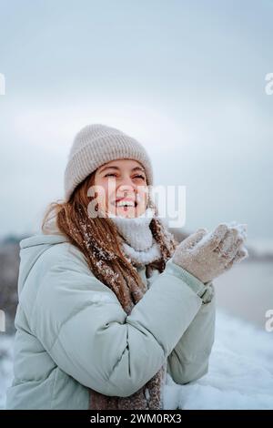 Happy woman wearing warm clothes and playing with snow in winter Stock Photo