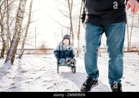 Father pulling boy sitting on sled in winter Stock Photo