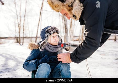 Father serving hot tea to son on snow in winter Stock Photo