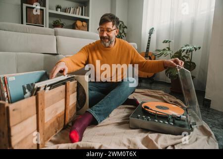 Man listening to vinyl records sitting with box full of disks at home Stock Photo