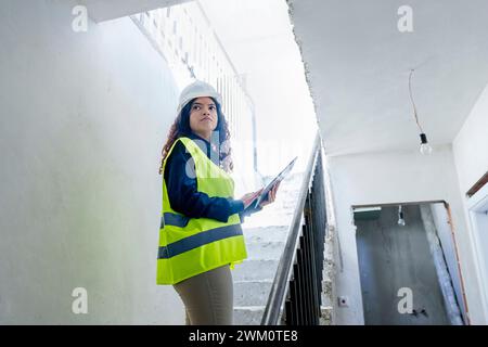 Young architect with blueprint standing on steps at construction site Stock Photo