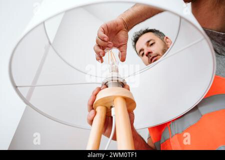 Electrician installing light bulb in lamp shade at home Stock Photo