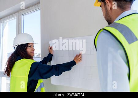 Young architect discussing over blueprint with colleague at site Stock Photo