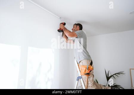 Repairman drilling hole in wall at home Stock Photo