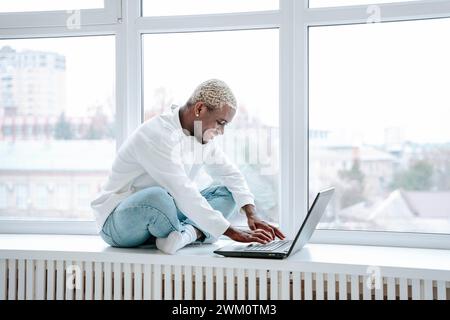 Happy freelancer using laptop near window Stock Photo