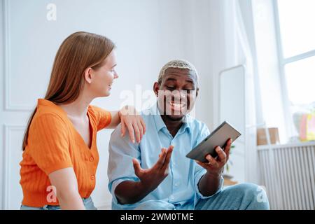 Happy young man discussing and holding tablet PC with woman at home Stock Photo