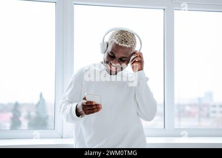 Happy young man wearing wireless headphones and using smart phone Stock Photo