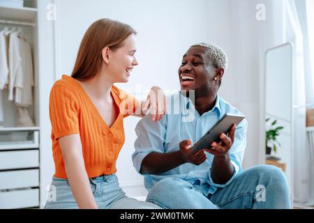 Cheerful young man discussing and holding tablet PC with woman at home Stock Photo