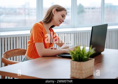 Smiling young freelancer using laptop near window Stock Photo