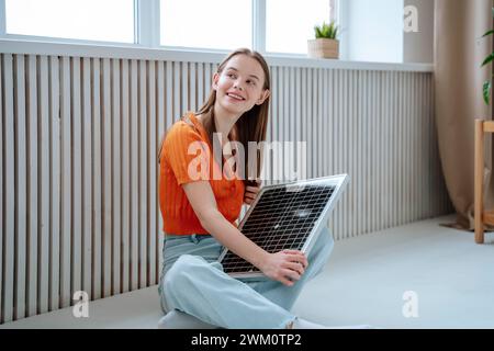 Smiling young woman sitting with solar panel at home Stock Photo