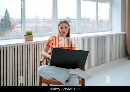 Smiling young freelancer sitting with laptop on armchair at home Stock Photo
