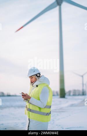 Engineer using smart phone standing in front of wind turbine Stock Photo