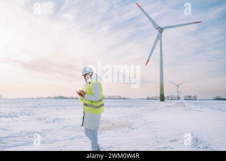 Engineer using smart phone standing at wind farm Stock Photo