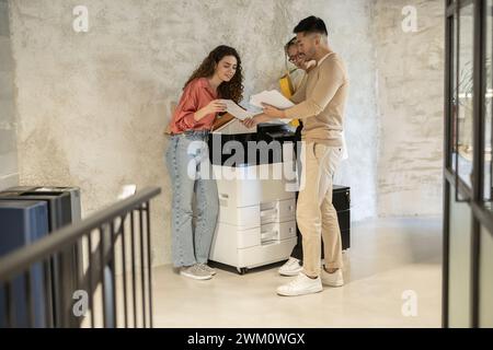 Young business colleagues discussing over documents standing by photocopier at office Stock Photo