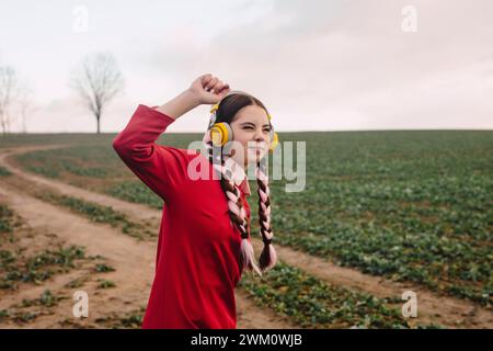 Smiling young woman wearing wireless headphones and enjoying at field Stock Photo