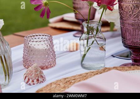 Picnic aesthetics table setting, flowers arrangement, shells close up. Cozy setup with flowers and candles. Stock Photo