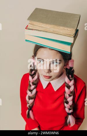 Woman balancing books on head near wall Stock Photo
