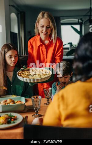 Smiling woman serving savory pie to family at Easter dinner Stock Photo