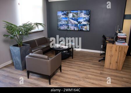 A stylish and modern office interior with dark gray walls, a large window and a monitor on the wall. comfortable leather furniture. Stock Photo