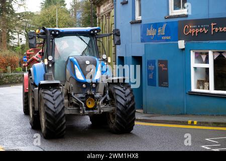 Blue tractor driving  along on Rhosmaen Street outside shops through the town of Llandeilo Carmarthenshire Wales UK Great Britain  2024 KATHY DEWITT Stock Photo