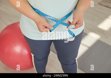 Overweight woman in sportswear is holding centimeter tape and measuring her waist Stock Photo