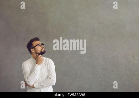 Man reflect on question or business problem looking aside standing on grey Stock Photo