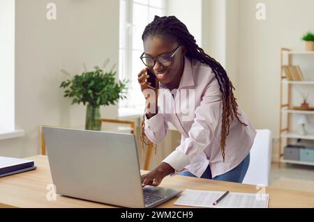 Happy smiling woman standing at the desk working at office and talking on mobile phone. Stock Photo