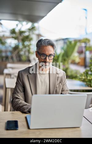 Middle aged business man executive sitting at outdoor table using laptop. Stock Photo