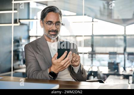 Busy mature business man entrepreneur sitting at desk using mobile cell phone. Stock Photo