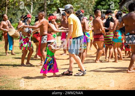 Tourist kid dancing with a local girl with santa claus hat on her head from Embera tribe in the jungle in Chagres national park, Panama Stock Photo