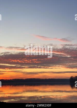 River Po and vibrant sunset in the background. The sky is painted in shades of orange, reflecting off the rippling water. San Nazzaro, PC, Italy Stock Photo